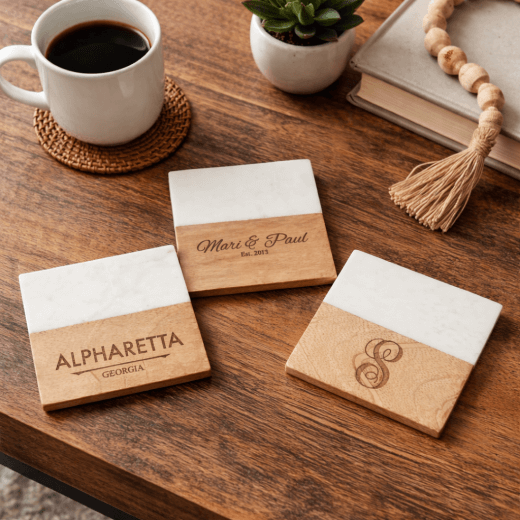 Three individual designer modern marble and wood table coasters personalized with text and monograms, styled on a dark wood table next to a coffee mug.