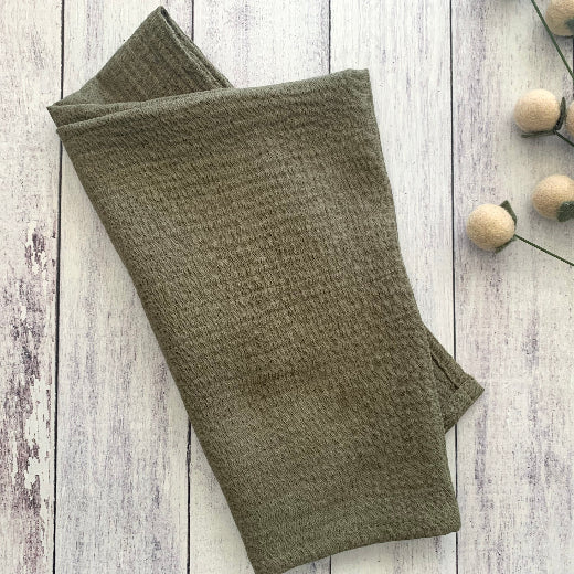 Folded Cotton Crinkle Napkins in mustard yellow, navy blue, burnt orange, olive green, sage green and dusty blue on a wooden surface.