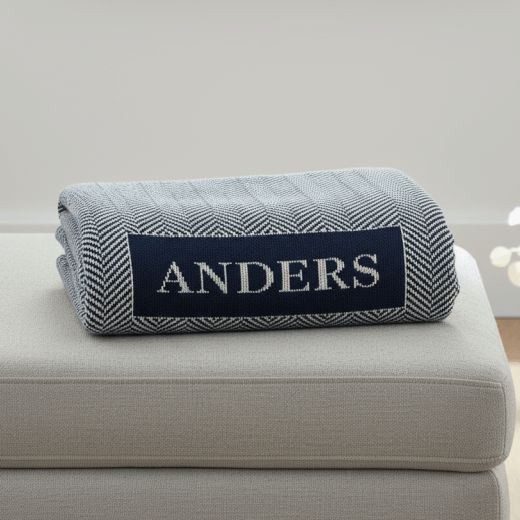 Navy and white herringbone blanket with the name Anders folded and sitting on an ottoman.