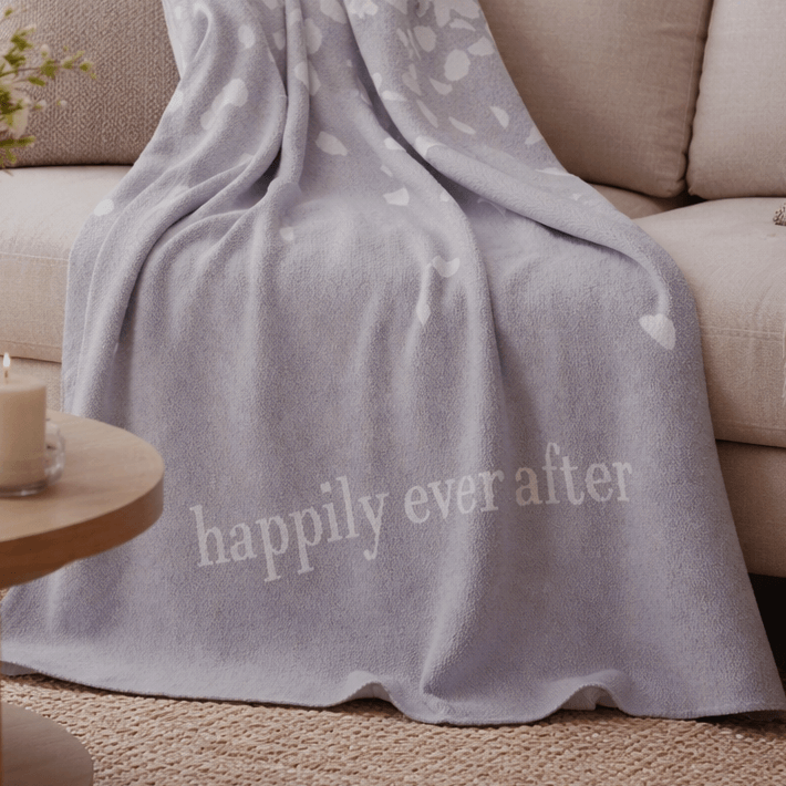Gray blanket with 'happily ever after' text draped over a beige couch.