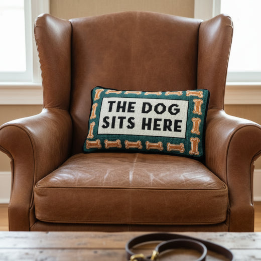 Dog Sits Here needlepoint pillow styled on a brown leather wingback chair