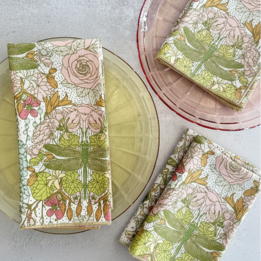 Floral and dragonfly patterned cloth napkins on a table with plates.