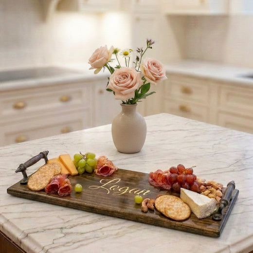 Personalized engraved wooden charcuterie tray with Logan script styled with cheese, grapes, and charcuterie on a marble kitchen island — custom serving tray from The Red Hound Gifts