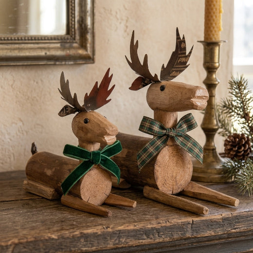 Two rustic wooden deer figurines made from cut logs, displayed on a wooden tabletop against a neutral beige background.