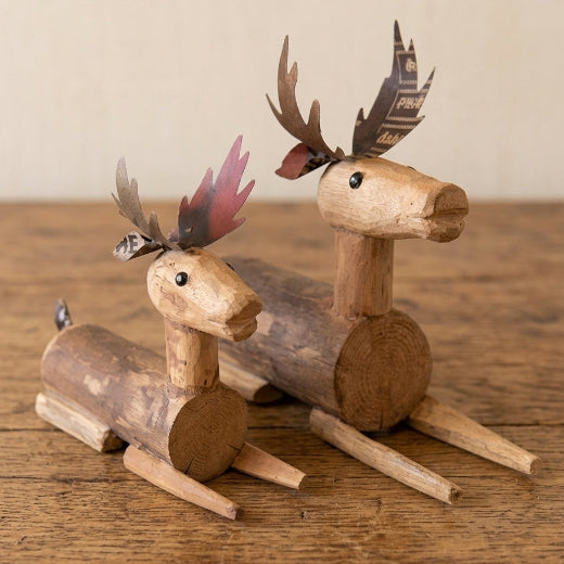 Two rustic wooden deer figurines made from cut logs, displayed on a wooden tabletop against a neutral beige background.