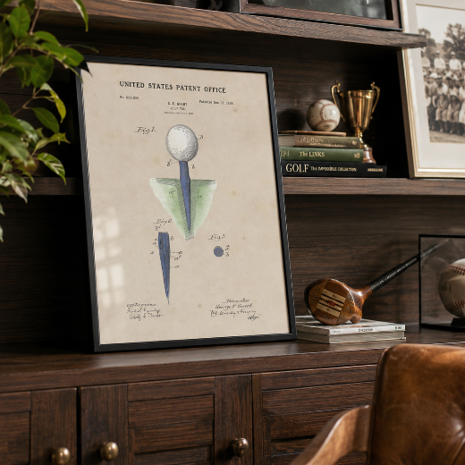 A framed vintage golf tee patent print featuring a golf tee with a white golf ball on a blue shaft, shown with a black frame against a light beige background.