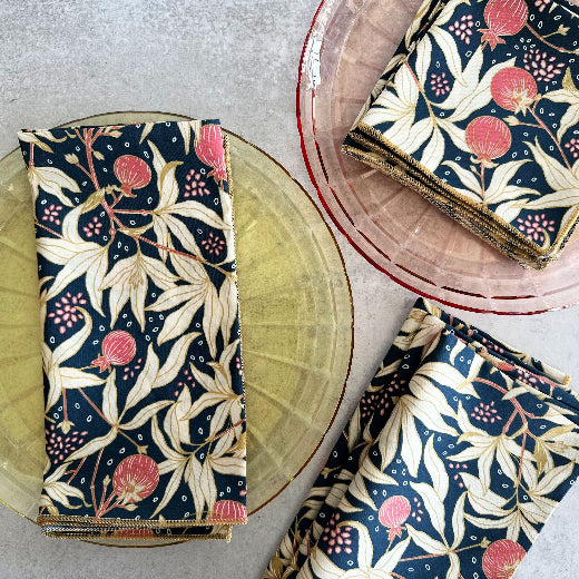 Floral cotton napkins featuring a navy background with gooseberry pinks and honey accents on a marble table with pink and yellow plates