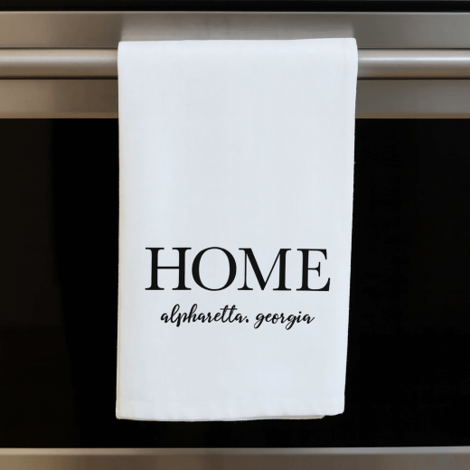 White cotton flour sack towel with 'HOME alpharetta, georgia' text hanging on an oven handle.