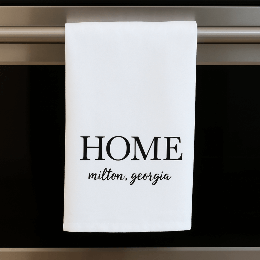 White cotton flour sack towel with 'HOME alpharetta, georgia' text hanging on an oven handle.