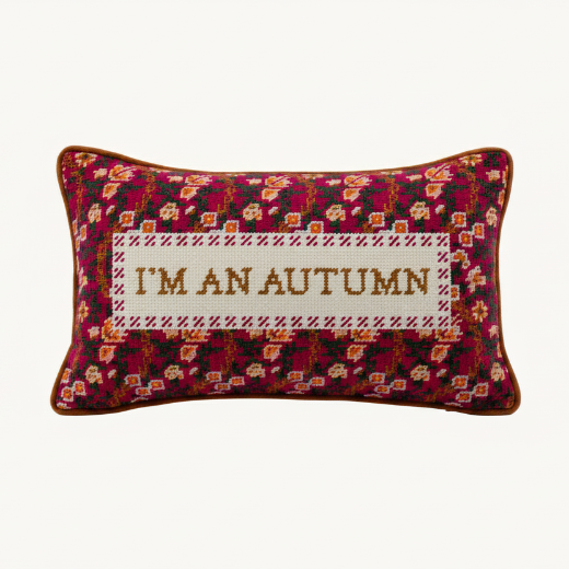 "I'm An Autumn" needlepoint pillow styled on a cream armchair with a golden orange throw blanket and dried floral arrangement. The Red Hound Gifts.