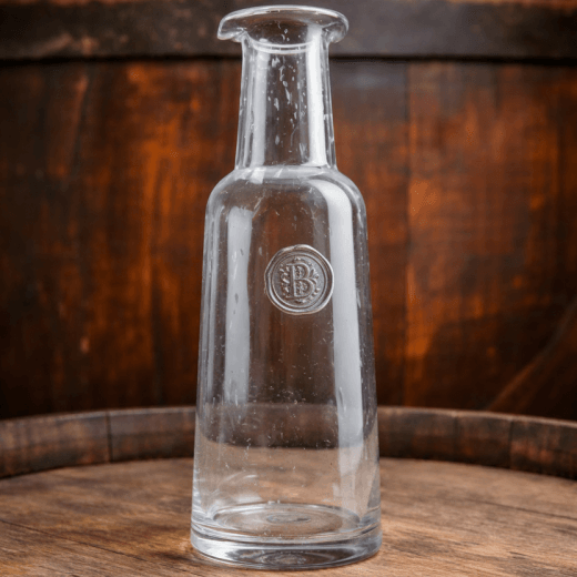 Clear glass bottle with a pewter initial medallion on a wooden surface