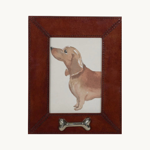 A brown leather picture frame with a bone-shaped metal hanger at the bottom and a watercolor illustration of a dachshund dog in the center.
