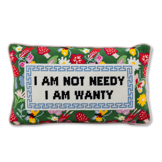 Needlepoint pillow with the phrase I am not needy I am wanty on a beige armchair in a home setting