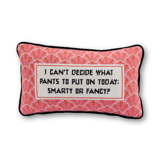 Decorative needlepoint pillow with I can't decide what pants to put on today: smarty or fancy text sitting on a beige armchair