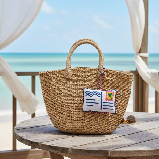 Needlepoint postcard bag charm with palm tree stamp detail, navy wave lines, and multicolor rope trim with gold tone lobster clasp