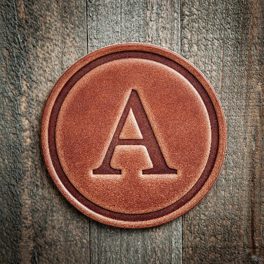 Signature leather initial coaster embossed with the letter A on a rustic wood surface — The Red Hound Gifts