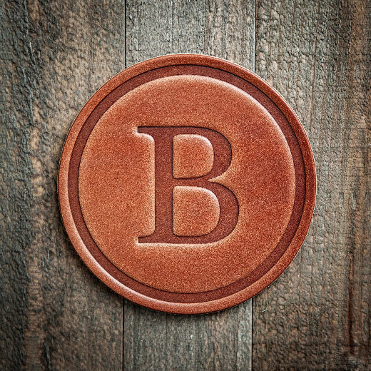 Signature leather initial coaster embossed with the letter B on a rustic wood surface — The Red Hound Gifts