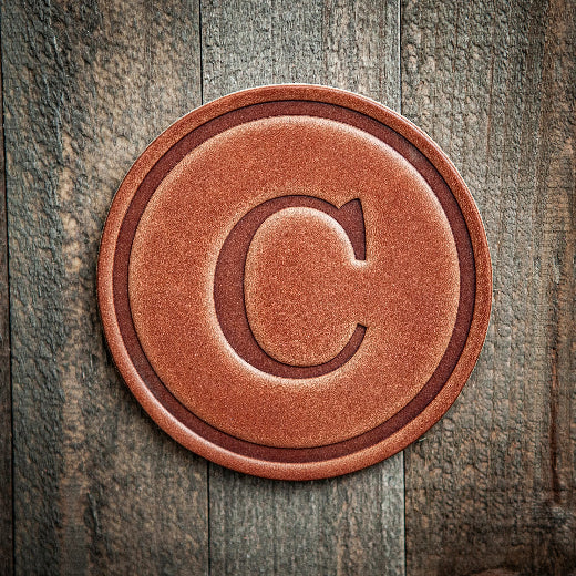 Signature leather initial coaster embossed with the letter C on a rustic wood surface — The Red Hound Gifts