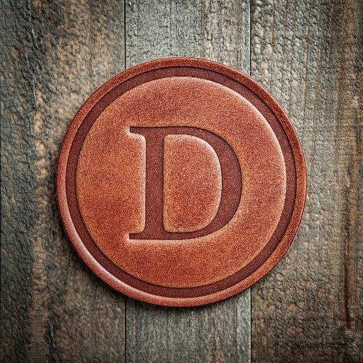 Signature leather initial coaster embossed with the letter D on a rustic wood surface — The Red Hound Gifts