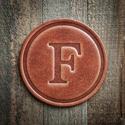 Signature leather initial coaster embossed with the letter F on a rustic wood surface — The Red Hound Gifts