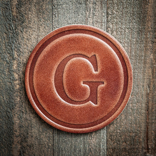 Signature leather initial coaster embossed with the letter G on a rustic wood surface — The Red Hound Gifts