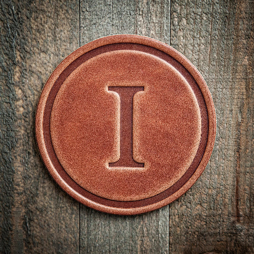 Signature leather initial coaster embossed with the letter I on a rustic wood surface — The Red Hound Gifts