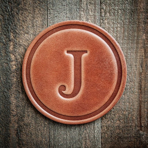 Signature leather initial coaster embossed with the letter J on a rustic wood surface — The Red Hound Gifts
