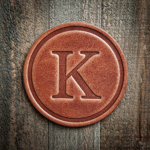 Signature leather initial coaster embossed with the letter K on a rustic wood surface — The Red Hound Gifts