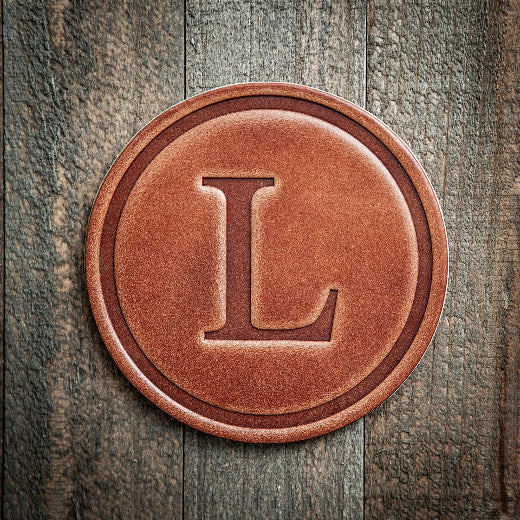Signature leather initial coaster embossed with the letter L on a rustic wood surface — The Red Hound Gifts