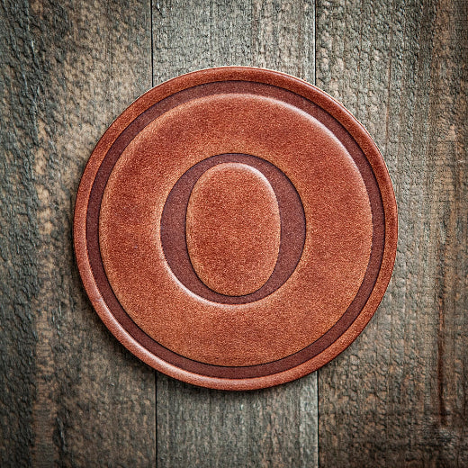 Signature leather initial coaster embossed with the letter O on a rustic wood surface — The Red Hound Gifts