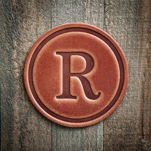 Signature leather initial coaster embossed with the letter R on a rustic wood surface — The Red Hound Gifts