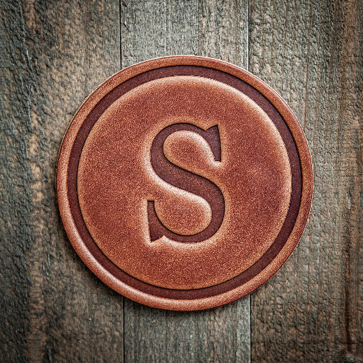 Signature leather initial coaster embossed with the letter S on a rustic wood surface — The Red Hound Gifts