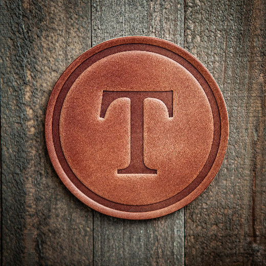 Signature leather initial coaster embossed with the letter T on a rustic wood surface — The Red Hound Gifts