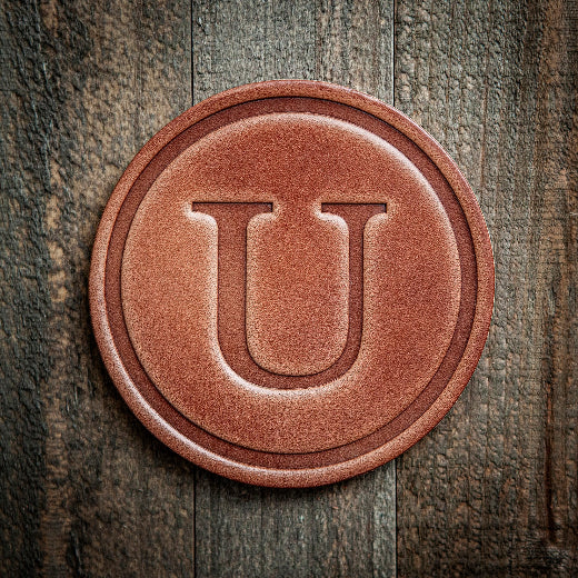 Signature leather initial coaster embossed with the letter U on a rustic wood surface — The Red Hound Gifts