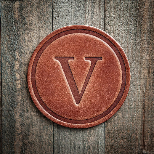 Signature leather initial coaster embossed with the letter V on a rustic wood surface — The Red Hound Gifts
