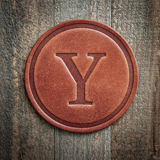 Signature leather initial coaster embossed with the letter Y on a rustic wood surface — The Red Hound Gifts