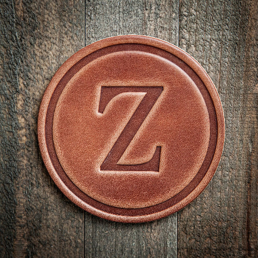 Signature leather initial coaster embossed with the letter Z on a rustic wood surface — The Red Hound Gifts