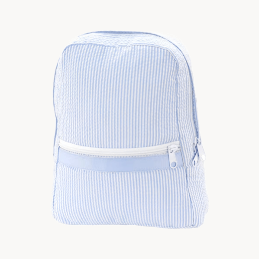 Pink backpack with 'Aria' embroidery, teddy bear, and wicker basket in the background