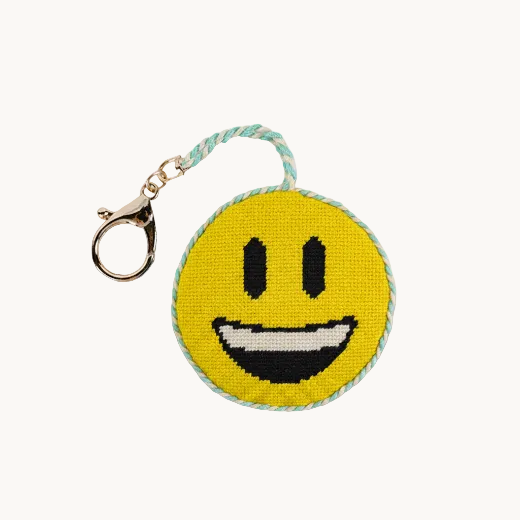 Needlepoint smiley face emoji bag charm in bright yellow with teal rope trim and a gold tone clasp