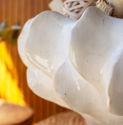 A white ceramic compote bowl with a ruffled rim, filled with pomegranates on a foyer table with sunglasses and keys sitting to the side of the bowl