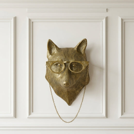 Antique brass finish fox wall mount wearing round spectacles with a draped chain on an off white background.