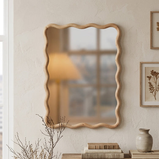 The Lottie wavy wood framed wall mirror styled in a warm neutral living room, hanging above a traditional wooden console table with books and a ceramic vase.