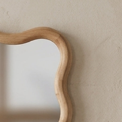 The Lottie wavy wood framed wall mirror styled in a warm neutral living room, hanging above a traditional wooden console table with books and a ceramic vase.