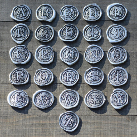 Clear glass bottle with a pewter initial medallion on a wooden surface